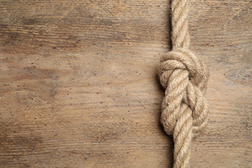 Top view of linen rope with knot on wooden background, space for text. Unity concept