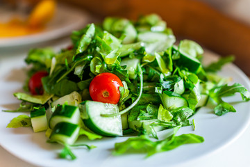 Closeup of fresh arugula cucumber salad on table in Italy with white plate and cherry tomato...