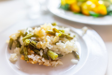 Closeup of cooked fried risotto Italian arborio rice with green beans on white plate and texture