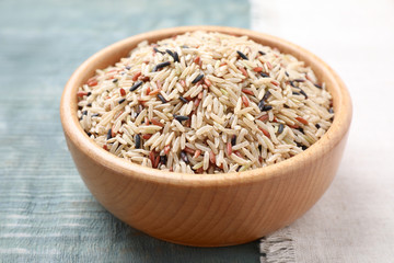 Mix of different brown rice in bowl on light blue wooden table