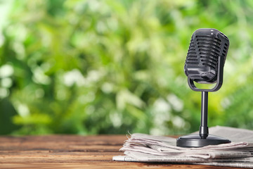 Newspapers and vintage microphone on wooden table against blurred green background, space for text....