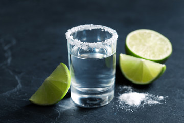 Mexican Tequila shot, lime slices and salt on grey table