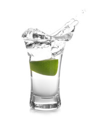 Splashing Mexican Tequila in shot glass with lime slice isolated on white