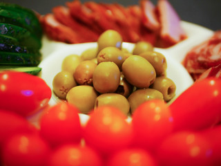 Vegetables and meat on one plate. A quick snack for guests. White plate against a dark background