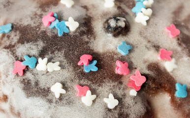 Sugar colored confetti lies on a white icing cupcake, texture of sugar icing on a cupcake surface close-up, pink, blue and white candy