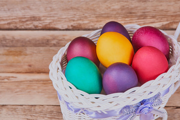 Easter composition. White basket on wheels with colorful Easter eggs on a wooden background. With copy space