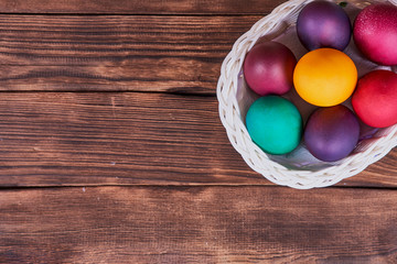 Easter composition. White basket on wheels with colorful Easter eggs on a wooden background. Flat lay