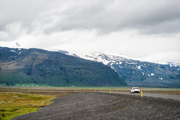 Fototapeta na wymiar Iceland mountains and car on ring road trip highway and snowcapped mountain cliff on cloudy day near Hof and Skaftafell national park