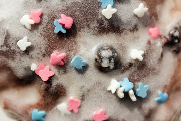 Sugar colored confetti lies on a white icing cupcake, texture of sugar icing on a cupcake surface close-up, pink, blue and white candy