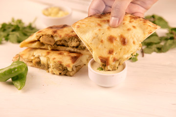 Hand dipping stuffed naan into sauce with green chillies on the side