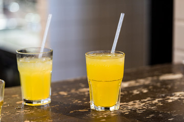 Closeup of two lemonade yellow juice drink cocktail glasses with plastic straws on table counter nobody