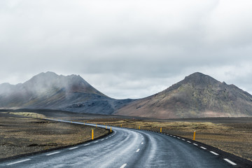 Ring road in east Iceland route 1 highway with barren bare brown landscape and rocky steep slope cliff with overcast cloudy stormy bad weather