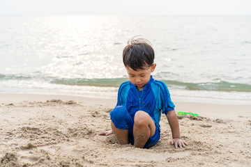 A boy is playing sand and swimming with his brother on the beach.