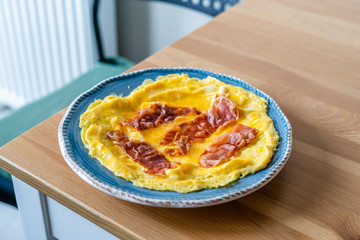 Omelette with Prosciutto Ham Jamon Crudo in Breakfast Plate on Wooden Kitchen Table.
