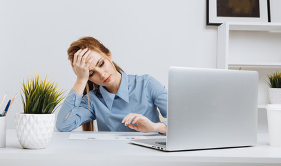 Young office girl sitting at her workplace feeling bad. Woman has a headache