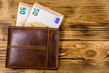 Brown leather wallet with fifty euro banknotes on the wooden background. Top view