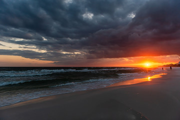 Fototapeta na wymiar Red orange, dramatic sunset in Santa Rosa Beach, Florida with coastline coast in panhandle with ocean gulf mexico waves during hurricane storm