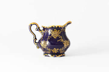 Closeup of a beautiful cobalt blue colored vintage porcelain tea milk jug with golden floral pattern on white background