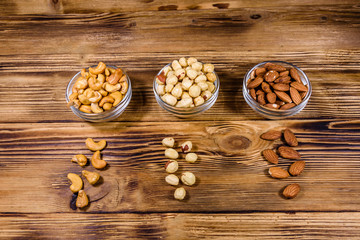 Various nuts (almond, cashew, hazelnut) in glass bowls on a wooden table. Vegetarian meal. Healthy eating concept