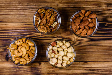 Various nuts (almond, cashew, hazelnut, walnut) in glass bowls on a wooden table. Vegetarian meal. Healthy eating concept. Top view