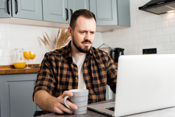 Guy with a cup of coffee is working on a laptop.