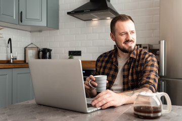 Guy with a cup of coffee is working on a laptop.