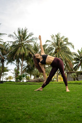  A girl practicing yoga on a beautiful tropical grass field surrounded by palm trees