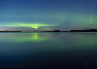 Northern lights dancing over calm lake. Farnebofjarden national park in Sweden.