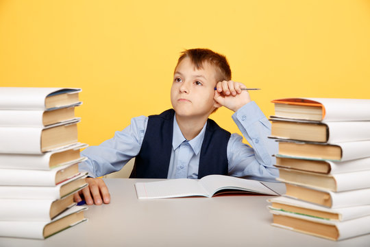 Thinking cute boy pupil in prosess of studying with a lot of books