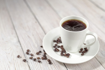 Close up a cup of hot coffee with roasted coffee beans on white wooden table.