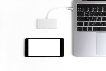 Laptop with usb-c hub on white desk. Black mobile phone with blank screen