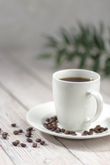 Close up a cup of hot coffee with roasted coffee beans on white wooden table.
