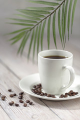 Close up a cup of hot coffee with roasted coffee beans on white wooden table.