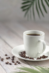 Close up a cup of hot coffee with roasted coffee beans on white wooden table.