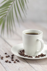 Close up a cup of hot coffee with roasted coffee beans on white wooden table.