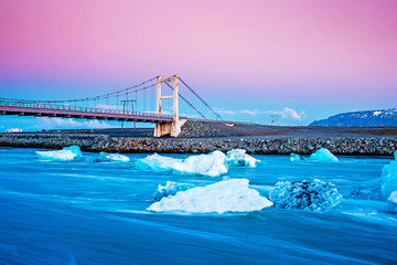 Fototapeta premium Iceberg parts float to the ocean under a bridge in the bay in the famous Jokulsarlon ice lagoon in Iceland. (global warming, greenhouse effect - concept)