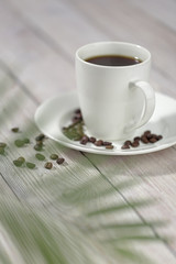 Close up a cup of hot coffee with roasted coffee beans on white wooden table.