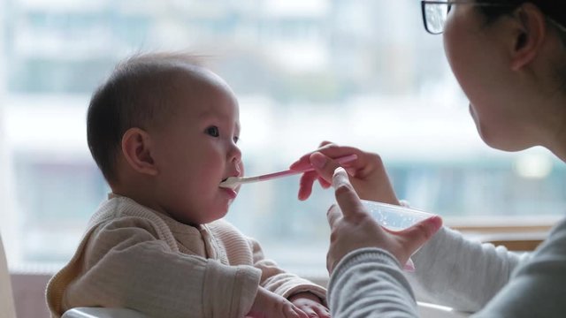 Slow motion asian mother feeding her baby daughter 9 month Chinese infant girl eating with spoon 