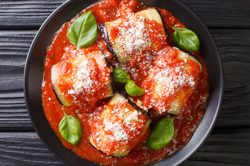 Tasty eggplant rolls stuffed with cheese and baked in tomato sauce close-up in a plate. Horizontal top view