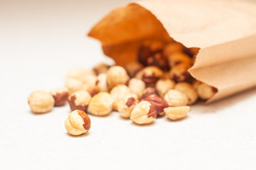 Poured beautifully laid out hazelnuts from a brown paper bag on a white table.