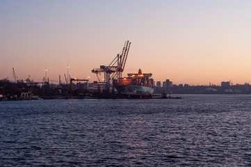 24-hour seaport work on loading container ships with cranes. Loading a large ship in the port at sunset.