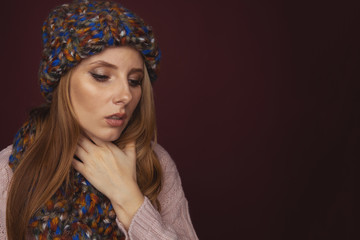 Sore throat concept. Closeup view of woman in sweater and hat with scarf holding her neck in pain
