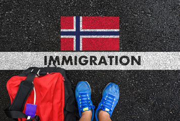 Man in shoes with bag standing next to line with word IMMIGRATION and flag of Norway  on asphalt...