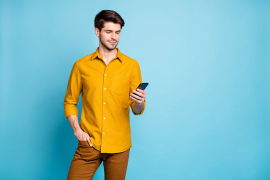 Photo Of Focused Handsome Bearded Man Wearing Yellow Shirt With Hand In Pocket Holding Telephone With Hand Reading Feed News Isolated Over Pastel Color Blue Background