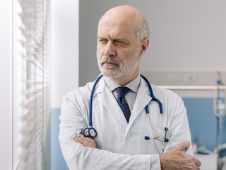 Confident chief physician standing next to a window and posing