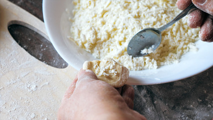 Mature female hands making dumplings with cheese at home kitchen, view from above.