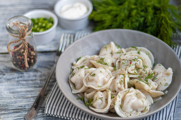 Boiled dumplings decorated with onions and peppers. In the background are greens, red peppers and bay leaves. On a light wooden background.