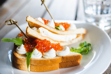 Classic breakfast, hot sandwich with red salmon caviar and mozzarella on a plate on a wooden table.