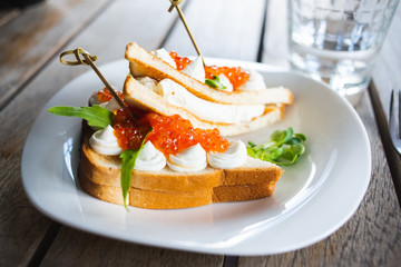 Classic breakfast, hot sandwich with red salmon caviar and mozzarella on a plate on a wooden table.