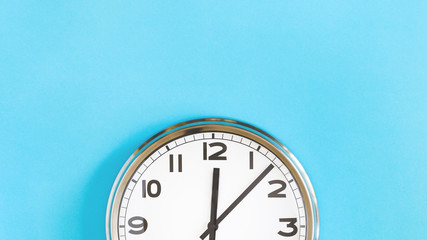 Top of big plain wall clock on pastel blue background. Five past twelve o'clock. Top view copy...